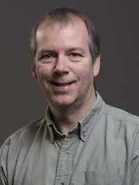 a man wearing an olive green shirt against a grey background