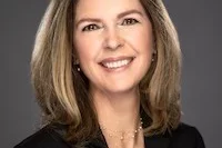 a brunette woman wearing a suit coat in front of a charcoal background