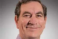 A man wearing a light purple shirt against a gradient dark background