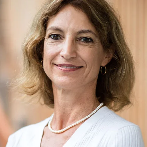 A woman with shoulder length hair, wearing a necklace and a white shirt