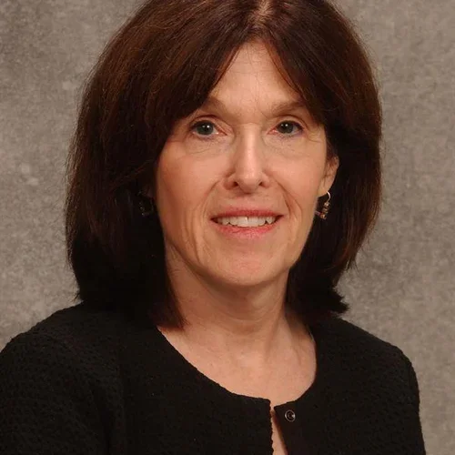 a woman with a black suit jacket against a beige background