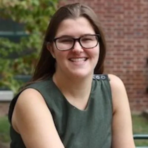 a woman in a green shirt sitting in front of a brick building 