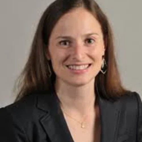 A woman with brown hair wearing a black suit jacket against a beige background