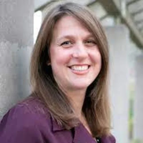 a woman with brown hair wearing a purple suit jacket in an outdoor setting