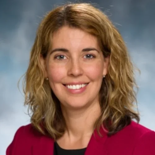 A woman with light curly hair wearing a red suit jacket