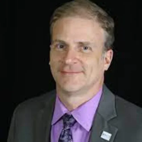 A man wearing a grey jacket with a purple shirt