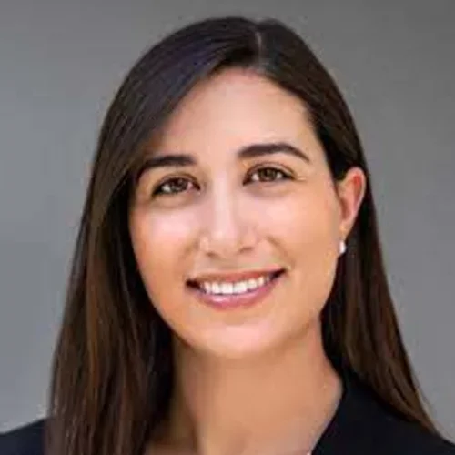 A woman with brown hair and brown eyes, wearing a black shirt,  smiling at the camera