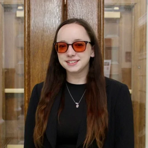 A woman with dark hair, wearing red glasses