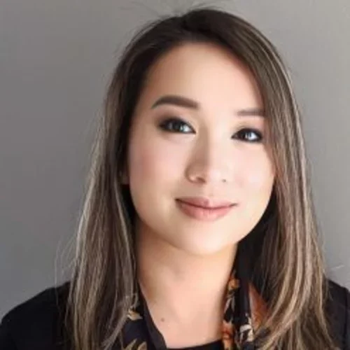 A woman with light brown hair, wearing a scarf with a black shirt, smiling against a dark grey background