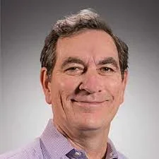 A man wearing a light purple shirt against a gradient dark background