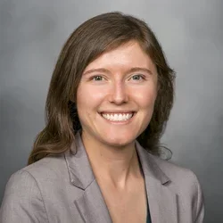 A woman with brown hair wearing a grey suit jacket