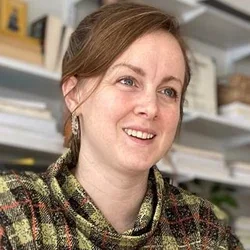 A woman with red hair, wearing a plaid sweater in a classroom
