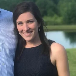 A woman with black hari, wearing earrings and a dark dress against a green background