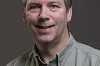 a man wearing an olive green shirt against a grey background