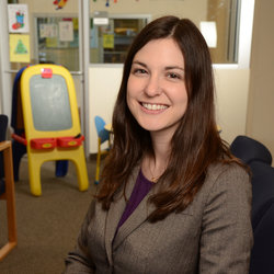 A brunette woman sitting down in a children's sensory room with toys, wearing a grey suit jacket.