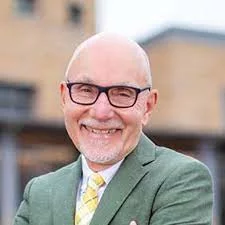 an older man wearing glasses and an olive green jacket with a plaid yellow tie