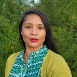 A woman with black hair, wearing a turquoise shirt with a green sweater